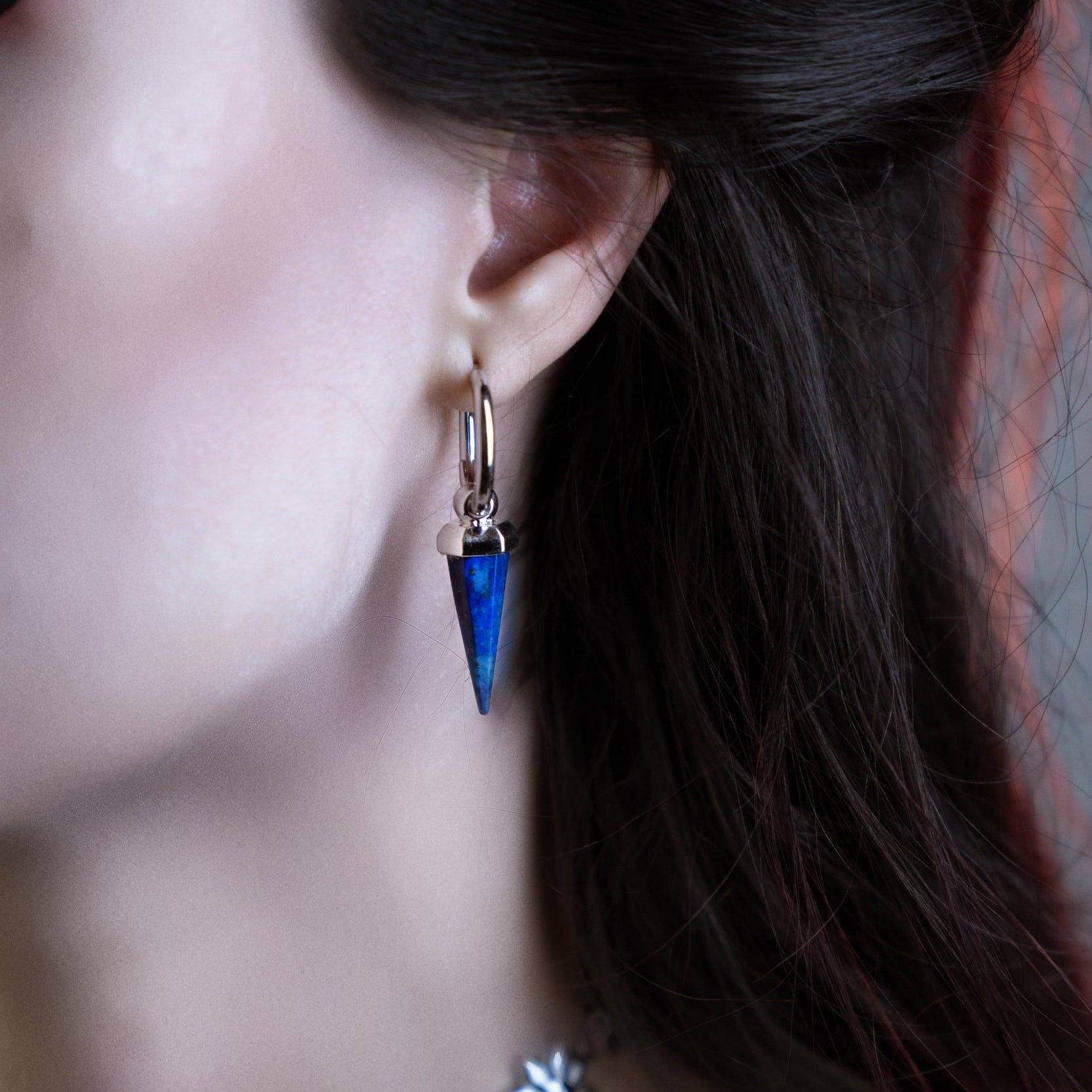 Close-up of a model wearing a silver-tone hoop earring with a blue crystal spike drop