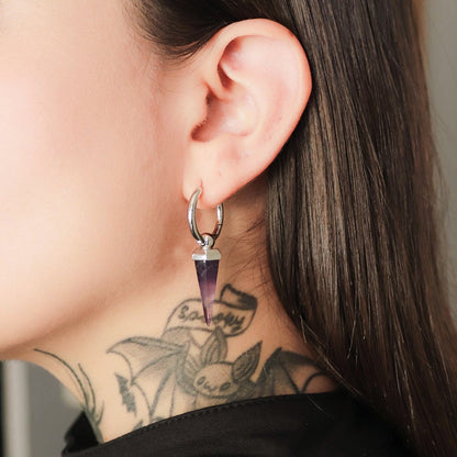 Close-up of a model wearing a silver-tone hoop earring with a purple crystal spike drop