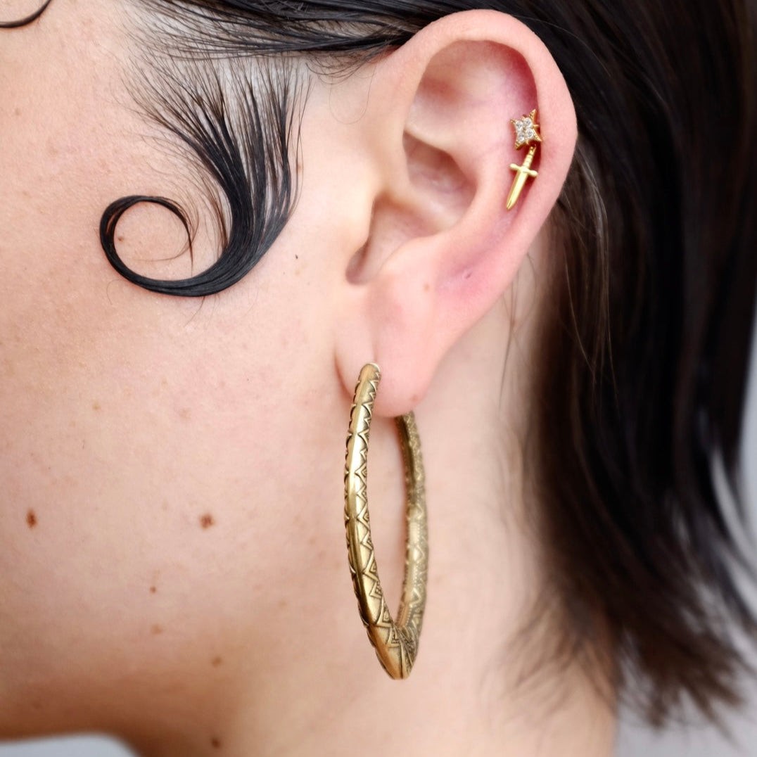 Close-up of a model wearing a textured gold-tone marquise hoop earring with a cross stud above