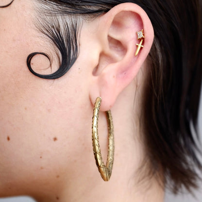 Close-up of a model wearing a textured gold-tone marquise hoop earring with a cross stud above