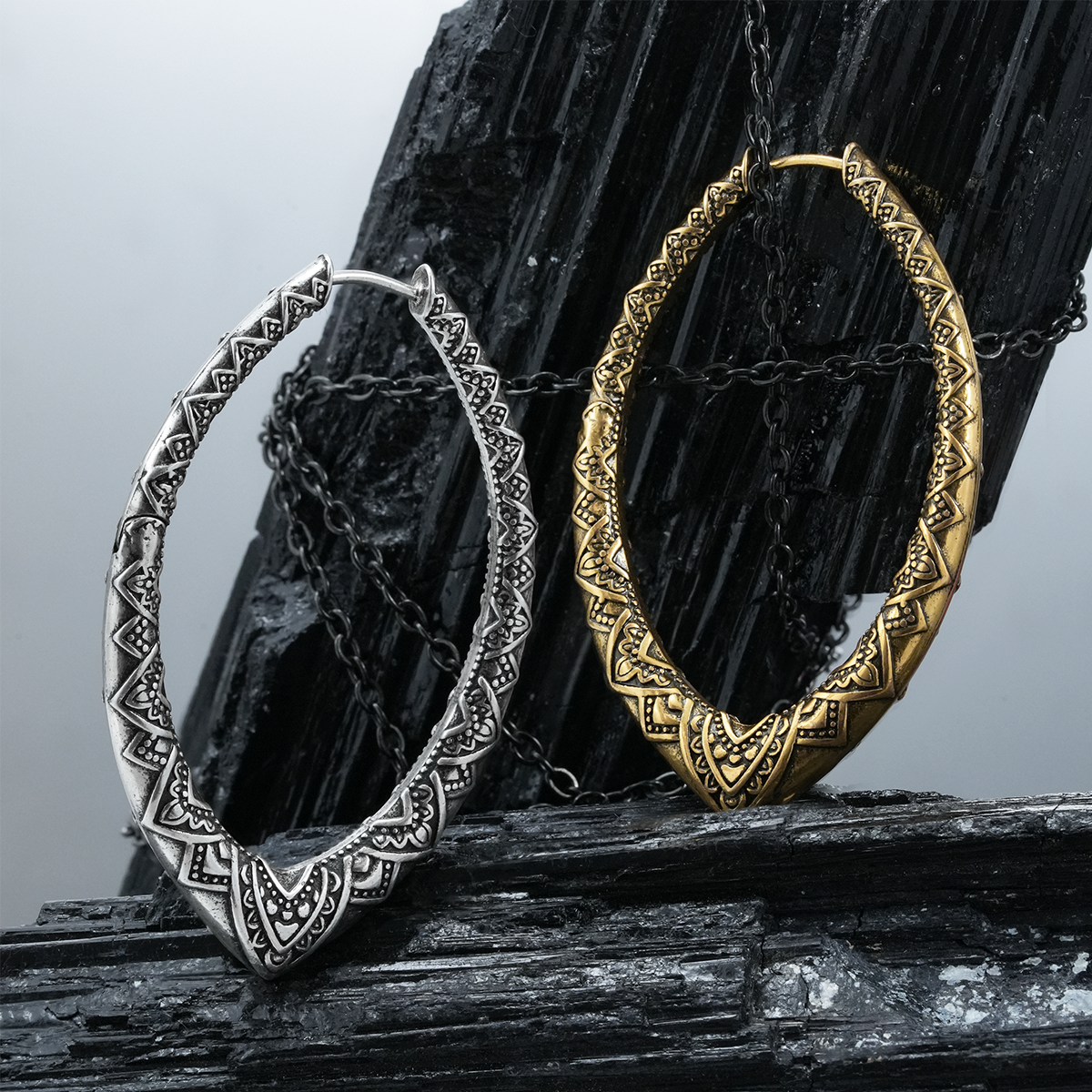 Silver and gold Cultural Essence hoop earrings displayed on black crystal