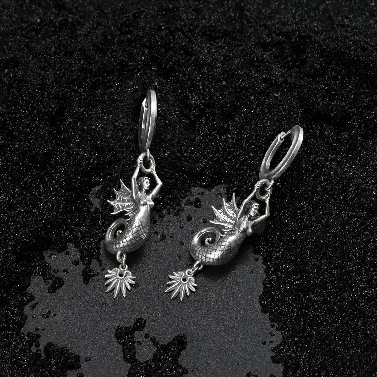 Dark coastal style silver siren earrings with a textured black sand background