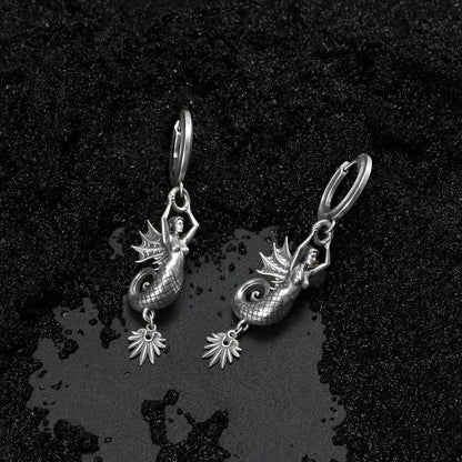 Dark coastal style silver siren earrings with a textured black sand background