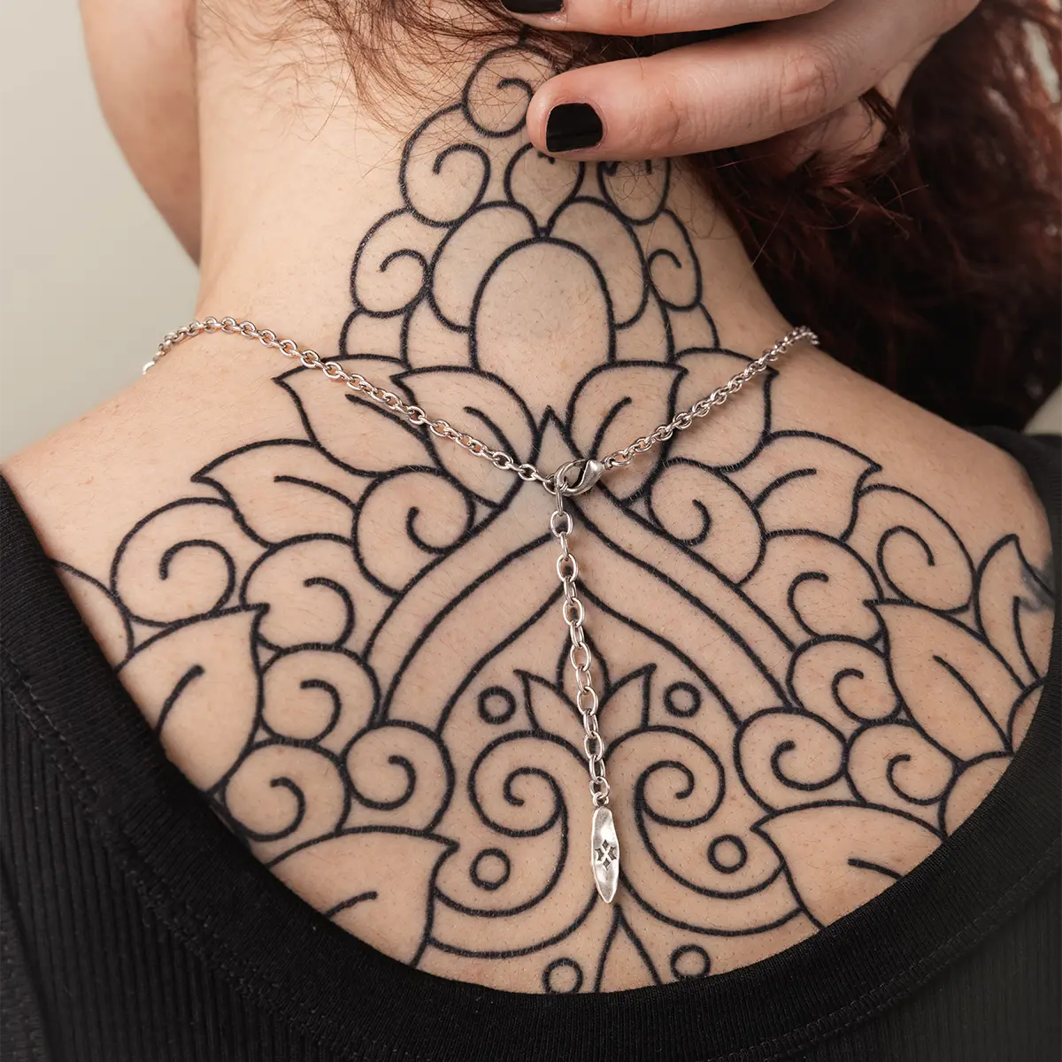 Dark romance jewelry aesthetic styled with a mythical tide knot necklace against a detailed back tattoo