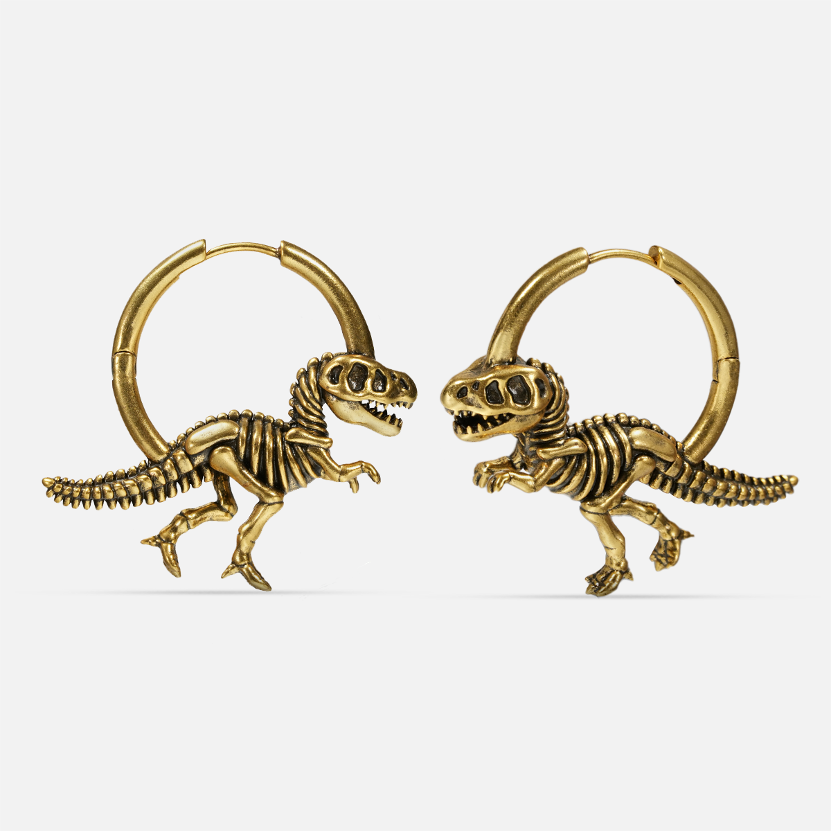 Pair of gold-tone hoop earrings featuring detailed dinosaur skeleton charms, shown side by side on a plain background