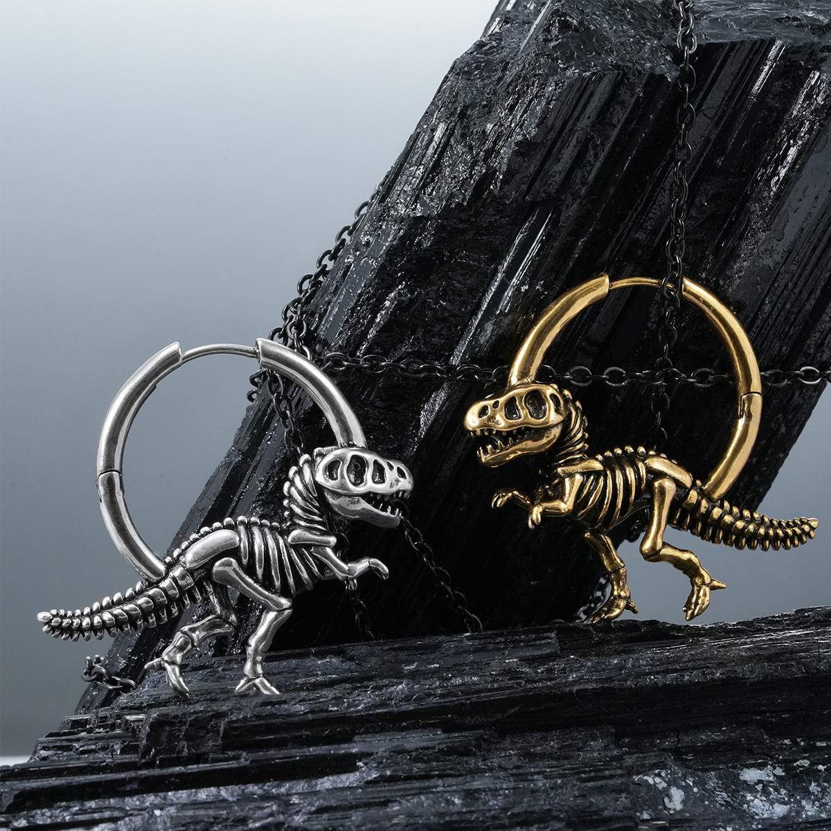 Silver-tone and gold-tone dinosaur skeleton hoop earrings displayed together on dark crystal rock formations