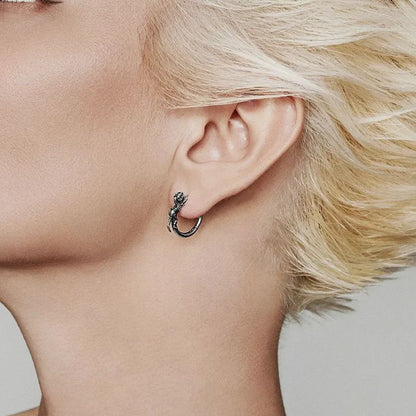 Dinosaur skeleton hoop earring in dark silver-tone worn on the ear, profile view against hair