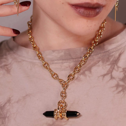 Model wearing the gold Dual Prism Necklace with a horizontal black crystal pendant, chunky chain, and structured gothic styling.