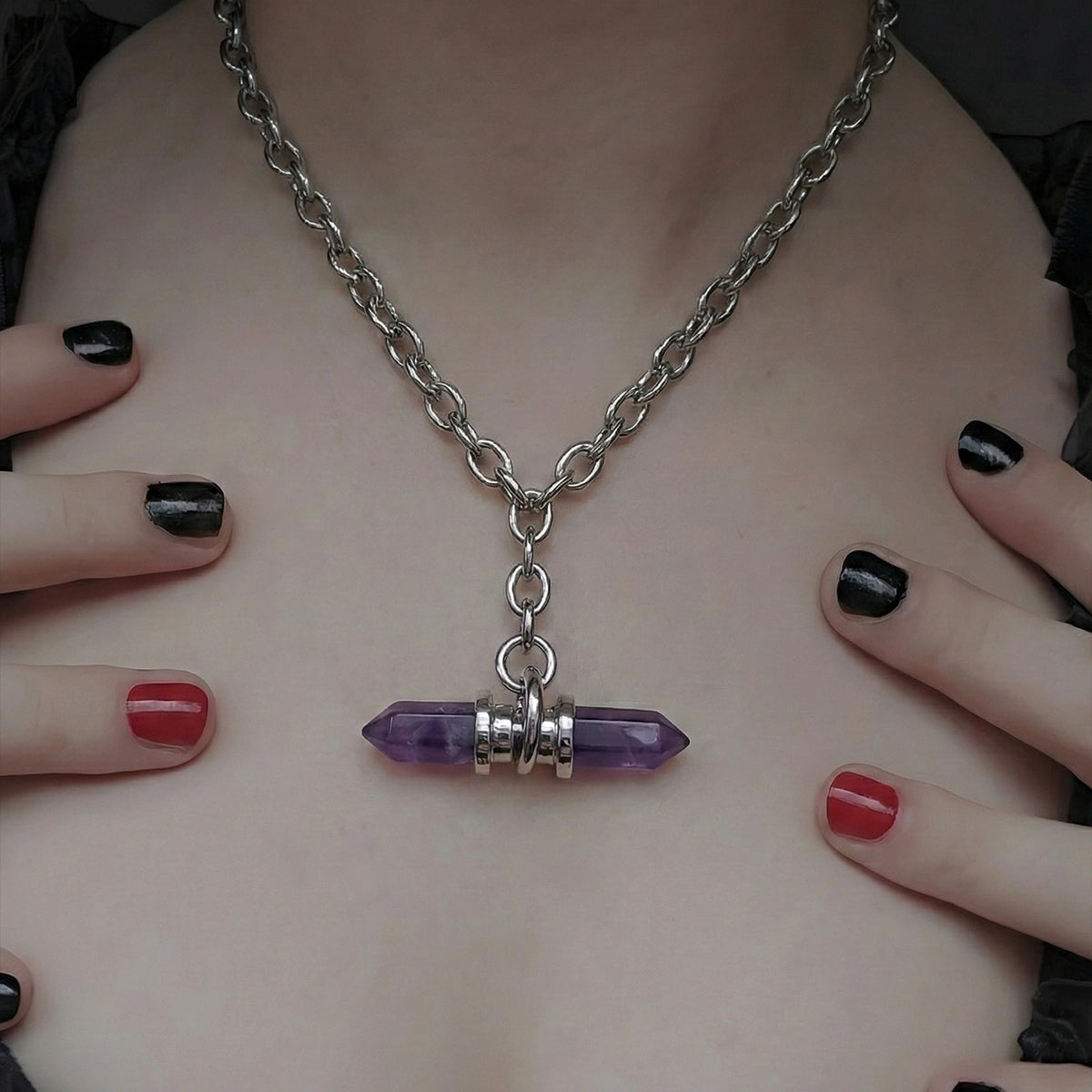 Silver-tone chain necklace with a purple crystal prism pendant worn around the neck, framed by hands with painted nails