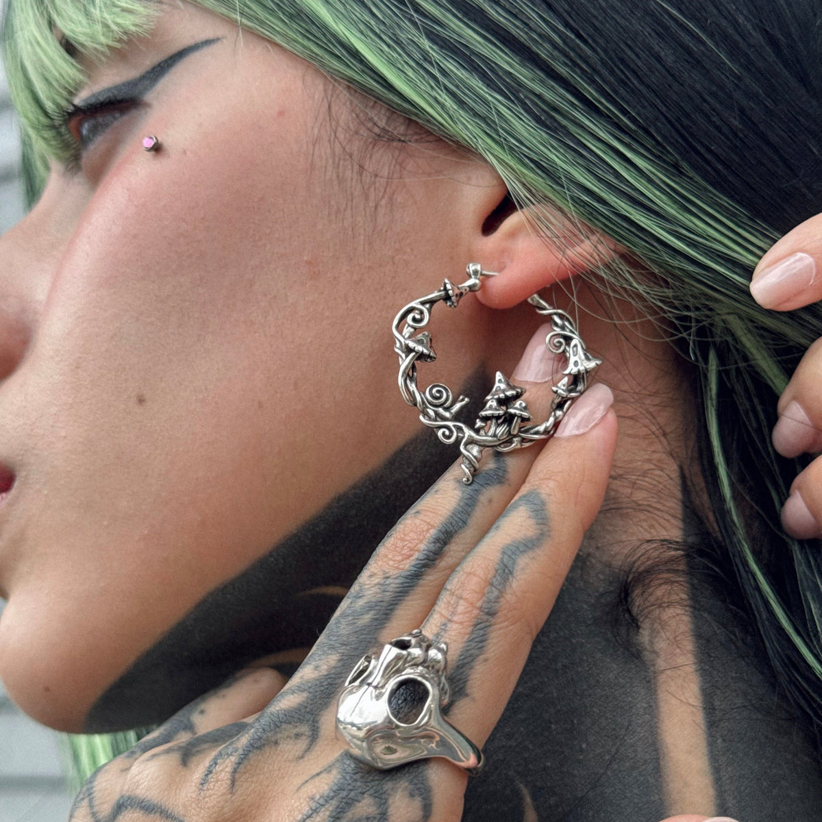 Model wears a silver-tone hoop earring with mushroom and vine details, shown in close-up profile view
