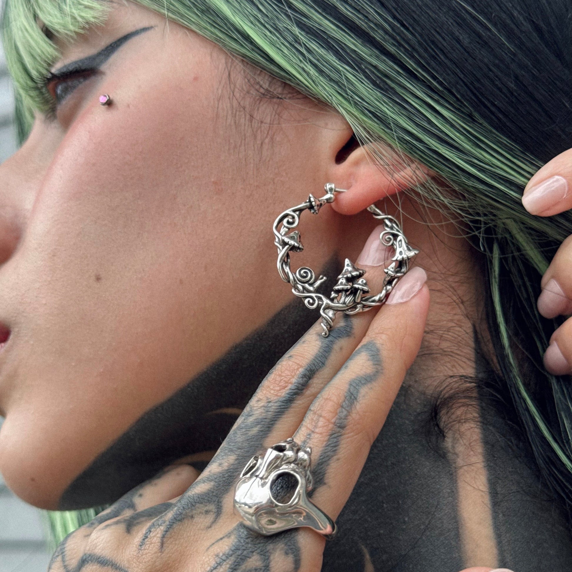 Model wears a silver-tone hoop earring with mushroom and vine details, shown in close-up profile view