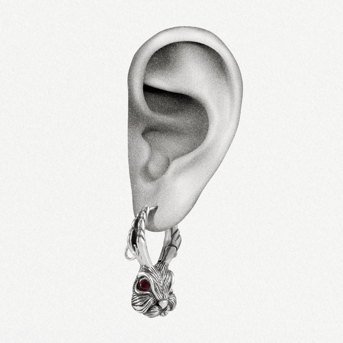 Silver-tone jackalope hoop earring with red gemstone eye worn on a model's earlobe, close-up view