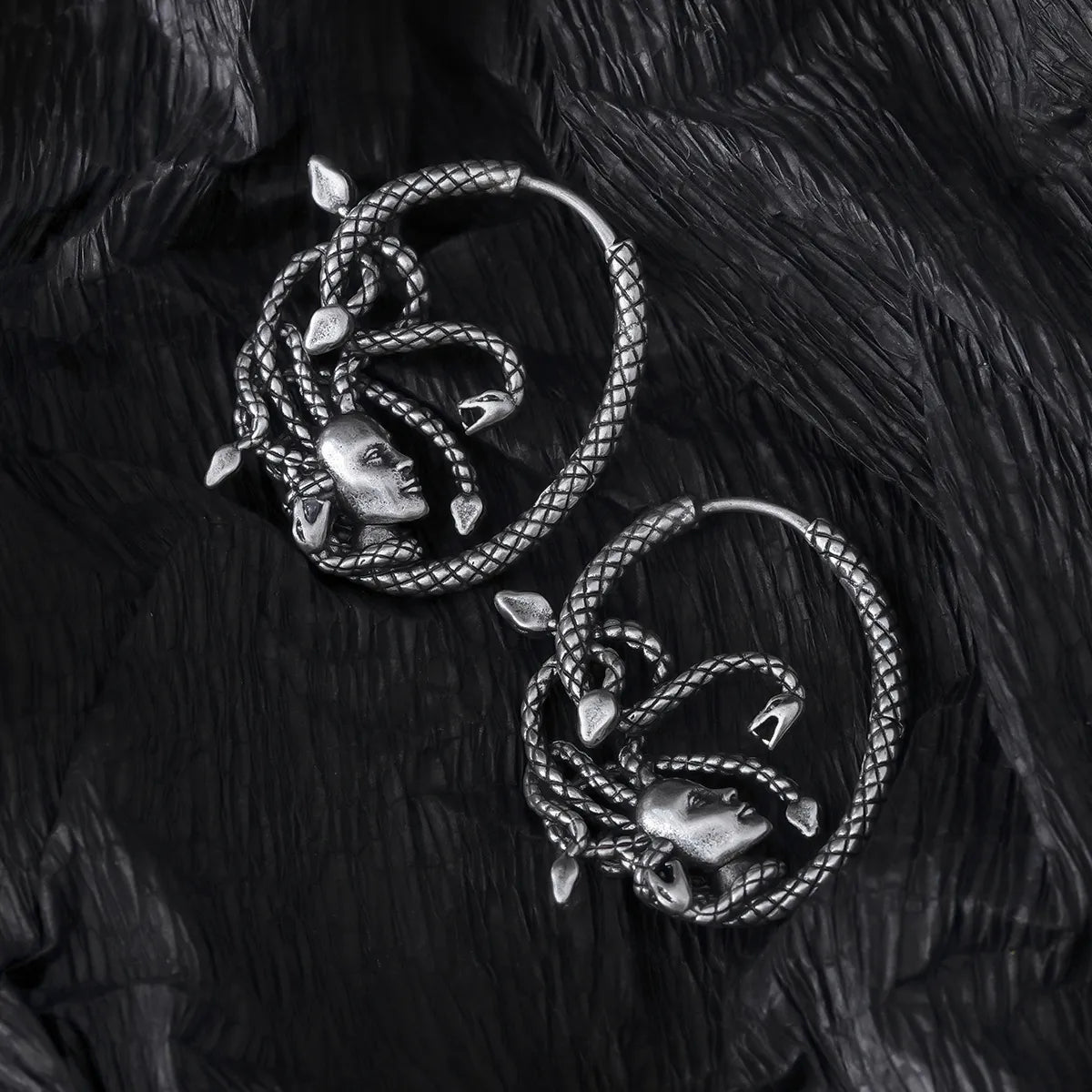 Pair of silver Enchanted Medusa hoop earrings displayed on black feathers