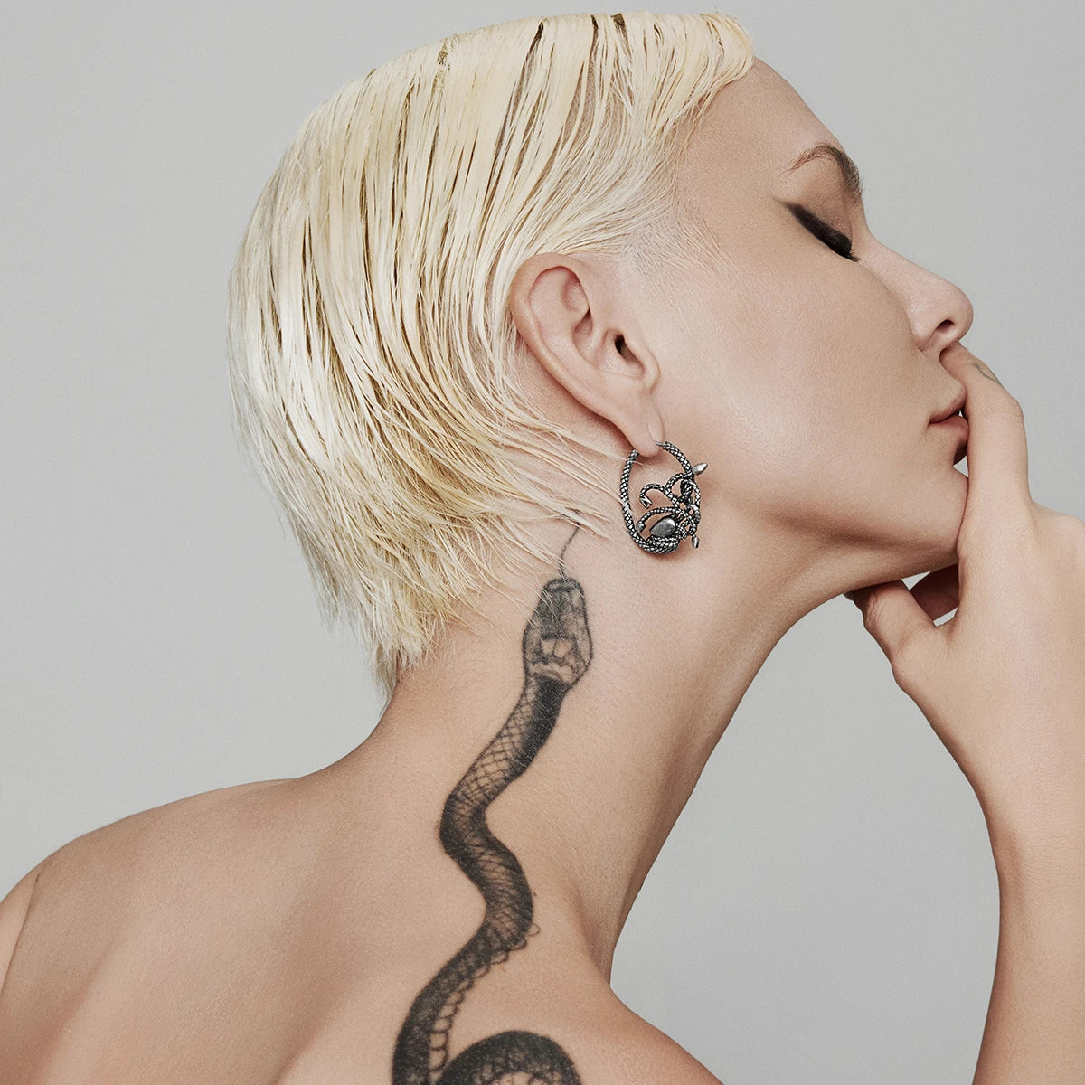 Model with short blonde hair wearing a silver-tone hoop earring featuring coiled snake detailing and a small face accent