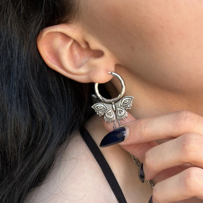 enchanted moth earrings shown on a model, featuring intricate moth silhouettes with all-seeing eye details in a close-up ear styling shot