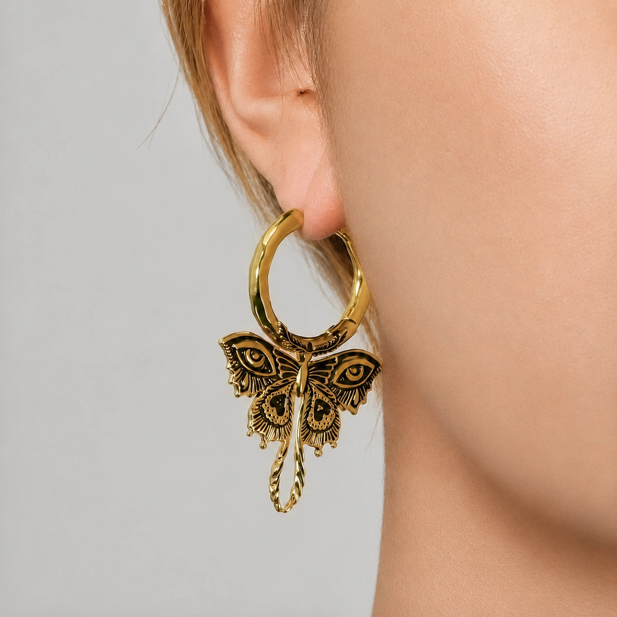 Gold-tone Enchanted Moth hoop earrings worn on two models, showing the dangling moth design from the side