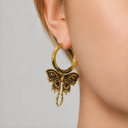 Gold-tone Enchanted Moth hoop earrings worn on two models, showing the dangling moth design from the side