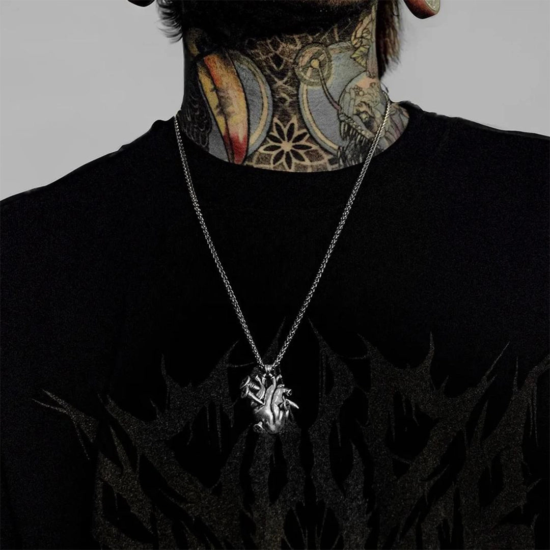 Silver-tone anatomical heart pendant on a chain necklace worn by a tattooed model in a black shirt