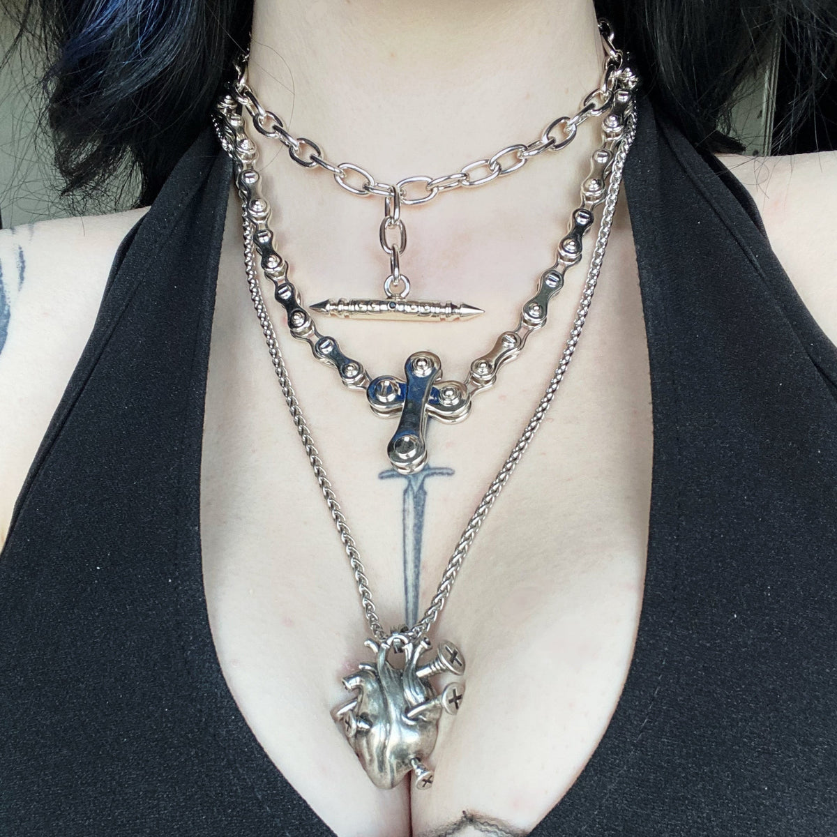 Layered silver-tone necklaces including a heart pendant, cross charm and bar charm worn over black top