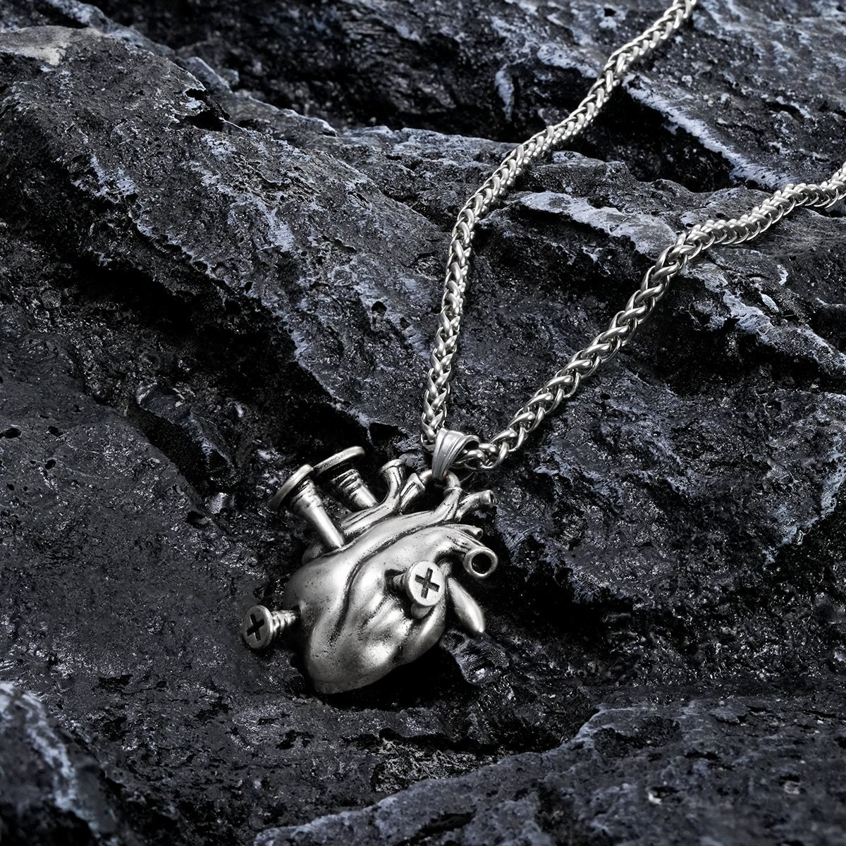 Silver-tone heart pendant necklace with chain laid across dark rock surface, close-up view