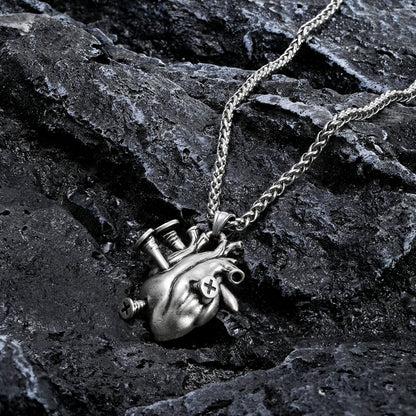 Silver-tone heart pendant necklace with chain laid across dark rock surface, close-up view