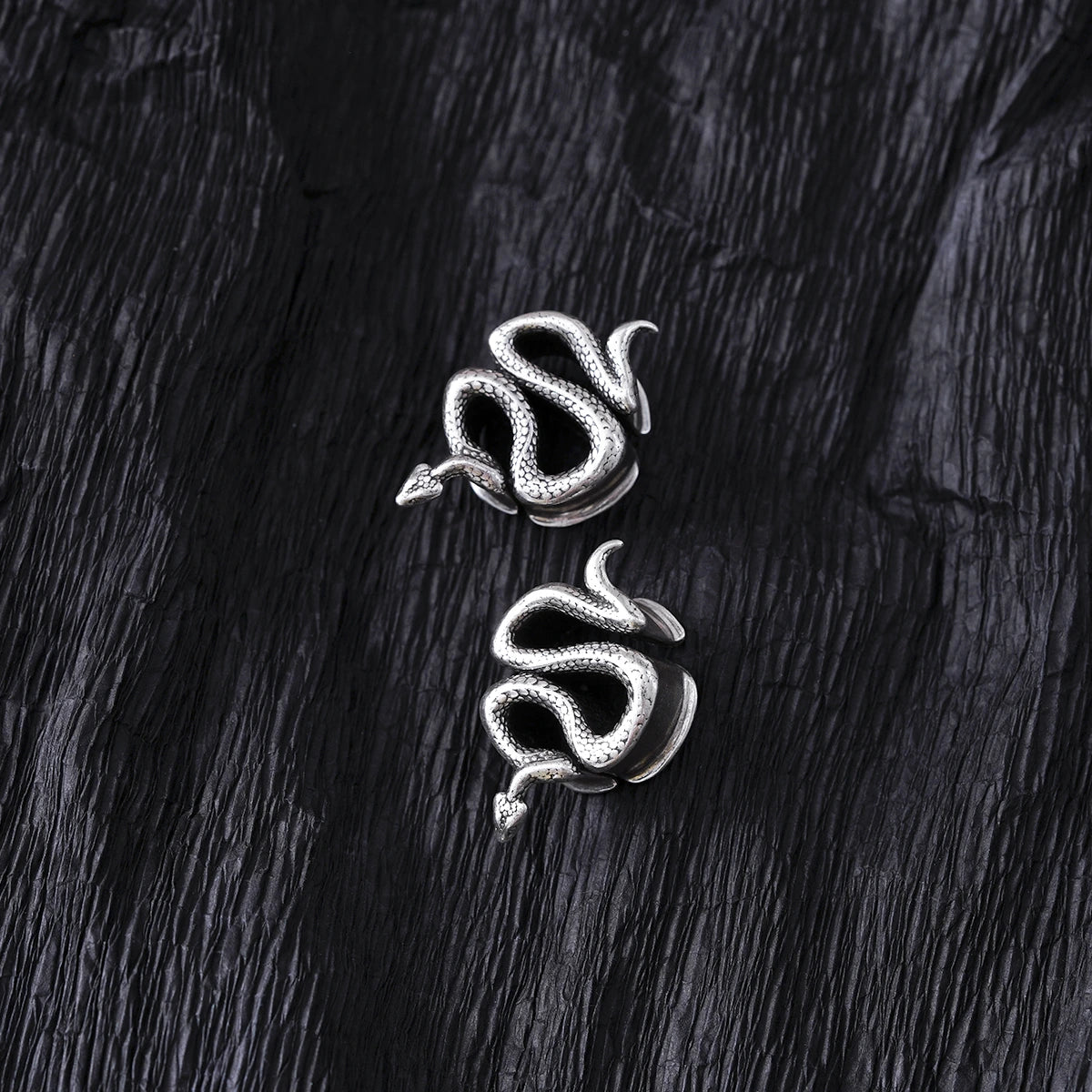 Pair of silver Enigmatic Serpent tunnels displayed on black feathers
