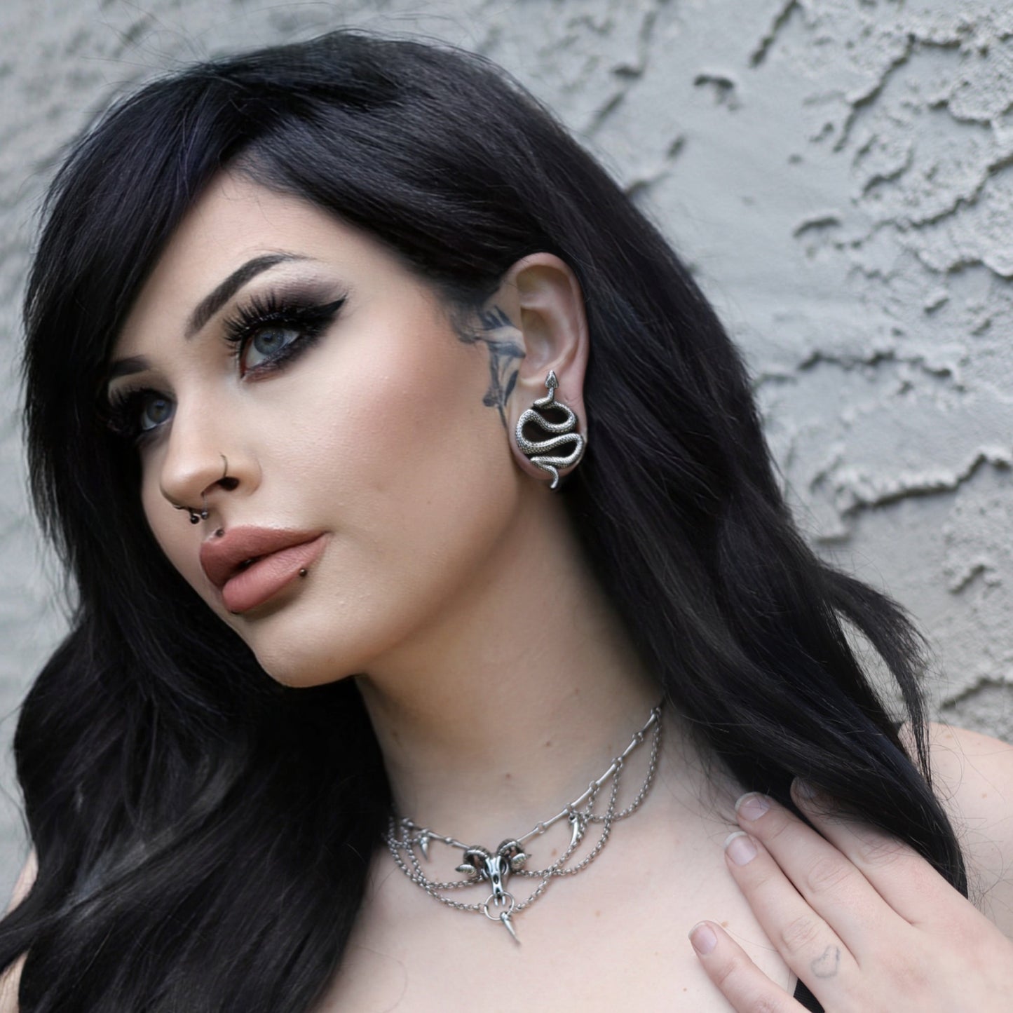 Model with dark hair wearing a silver-tone serpent tunnel earring and layered chain choker