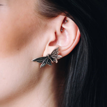 eternal moth ear studs shown in a model close-up view, featuring silver moth-shaped ear studs worn on the ear