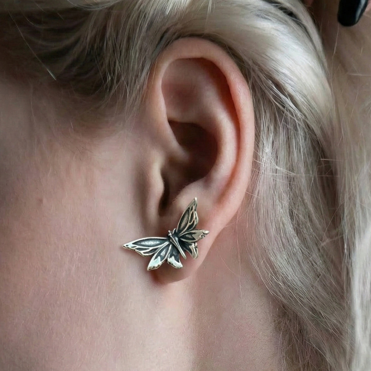 Close-up of a silver Eternal Moth ear stud worn on the earlobe