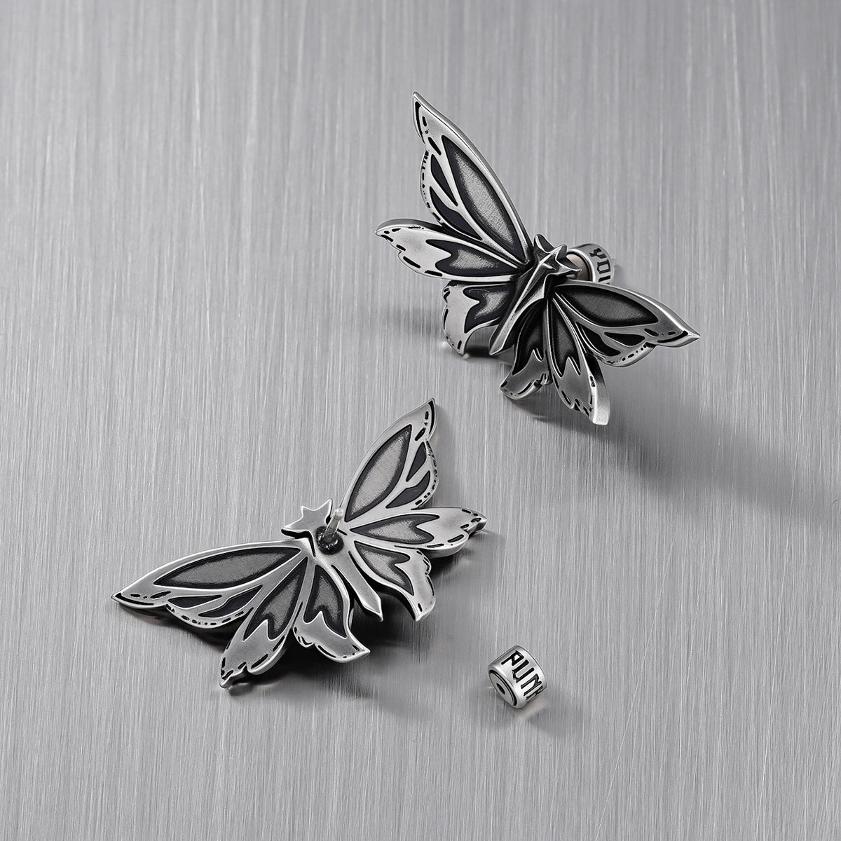 Pair of silver Eternal Moth ear studs with one removable backing visible