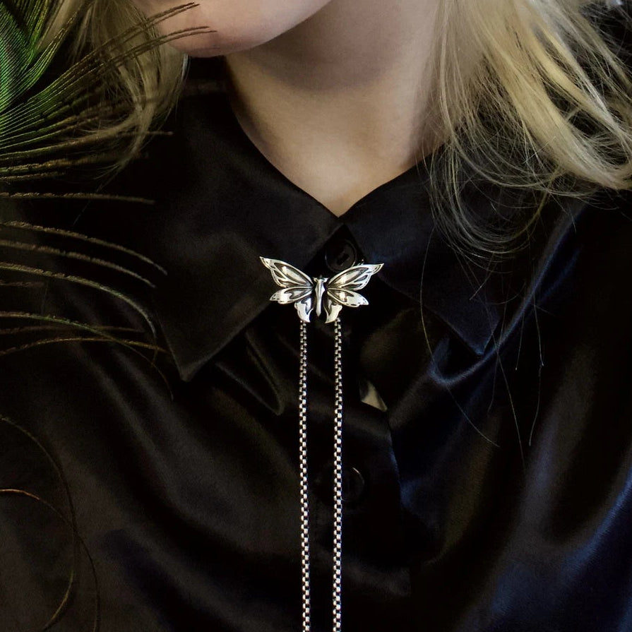 eternal moth necklace shown on a model, featuring sculpted moth wings and long chain drops in a dark editorial look