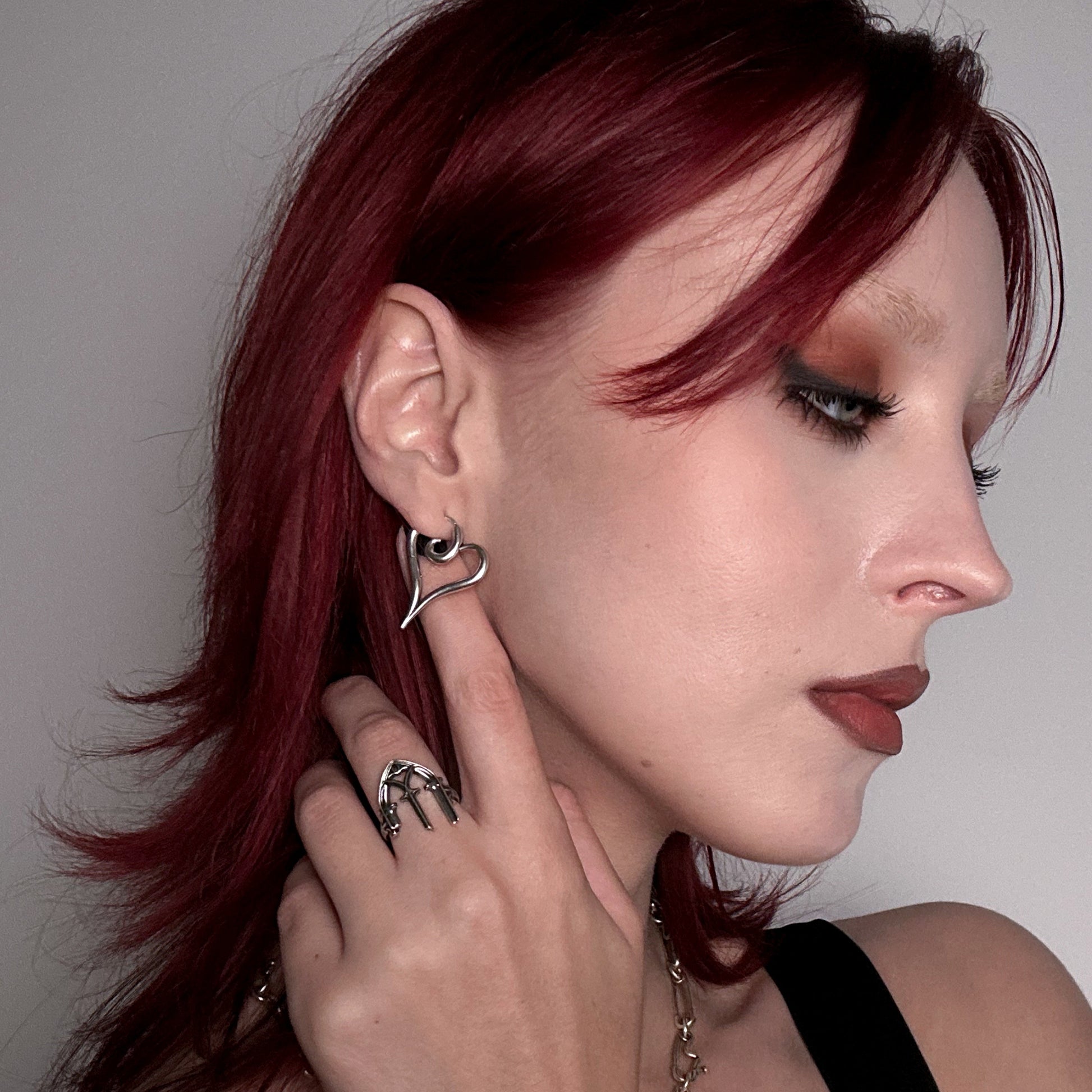 Silver-tone heart-shaped earring worn by a model with red hair, paired with a textured silver-tone ring