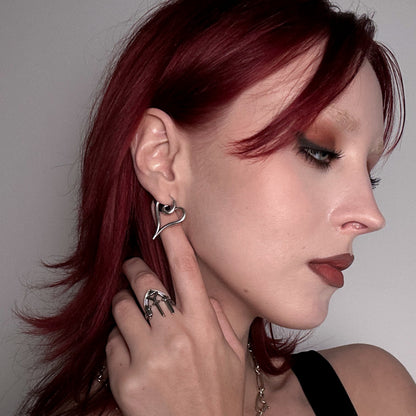 Silver-tone heart-shaped earring worn by a model with red hair, paired with a textured silver-tone ring
