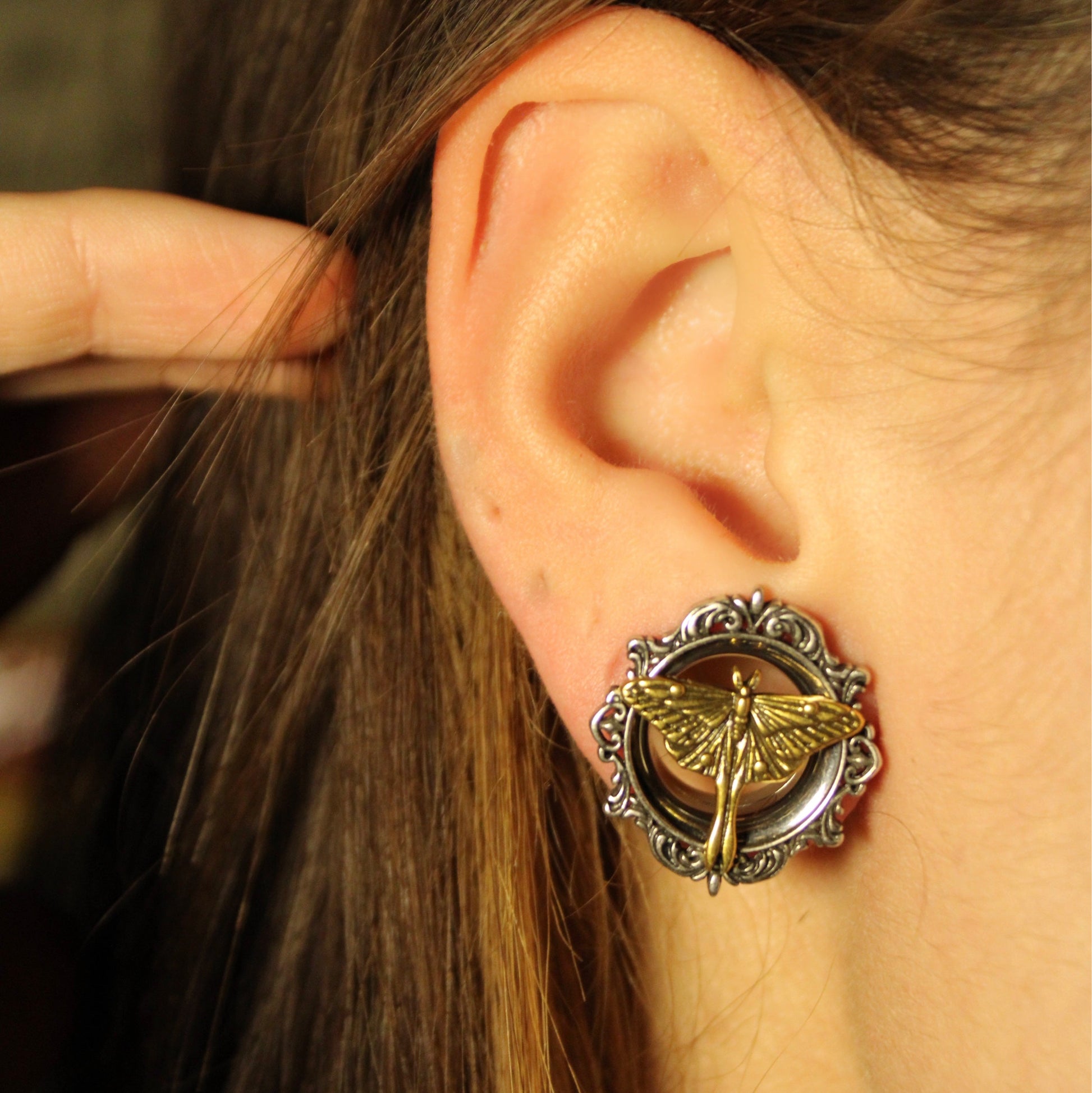 Close-up of an ear wearing a scrolled silver-tone tunnel with gold-tone moth motif, hair pulled back