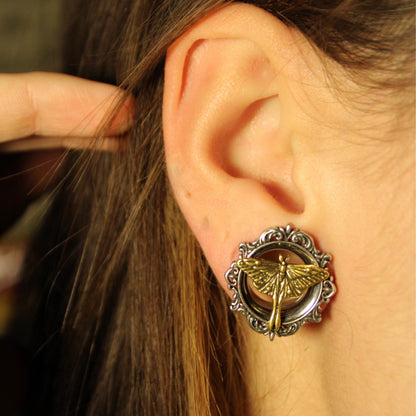 Close-up of an ear wearing a scrolled silver-tone tunnel with gold-tone moth motif, hair pulled back