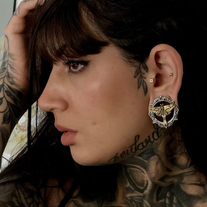 Tattooed model wears an ornate silver-tone ear tunnel with gold-tone moth design in lobe, profile view