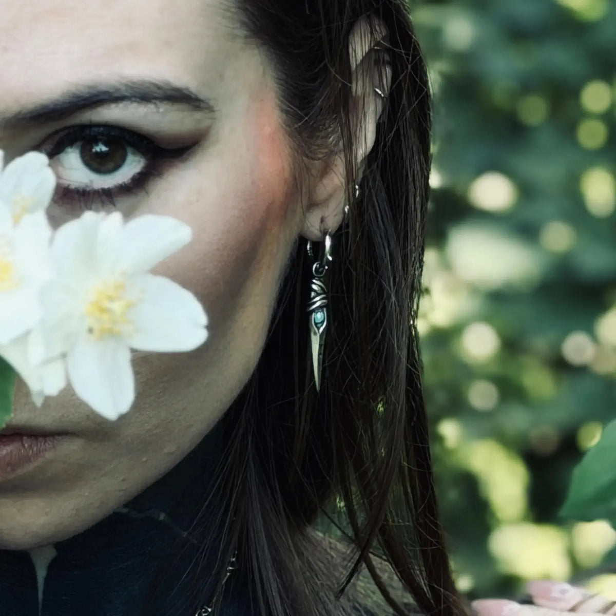 Eye Dagger Earrings in 925 sterling silver, worn in a close woodland portrait with white flowers in the foreground and the da