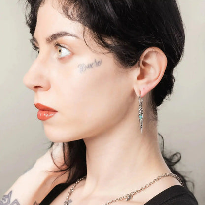 Eye Dagger Earrings in 925 sterling silver, worn in side profile with short dark hair, visible tattoos, and the turquoise eye