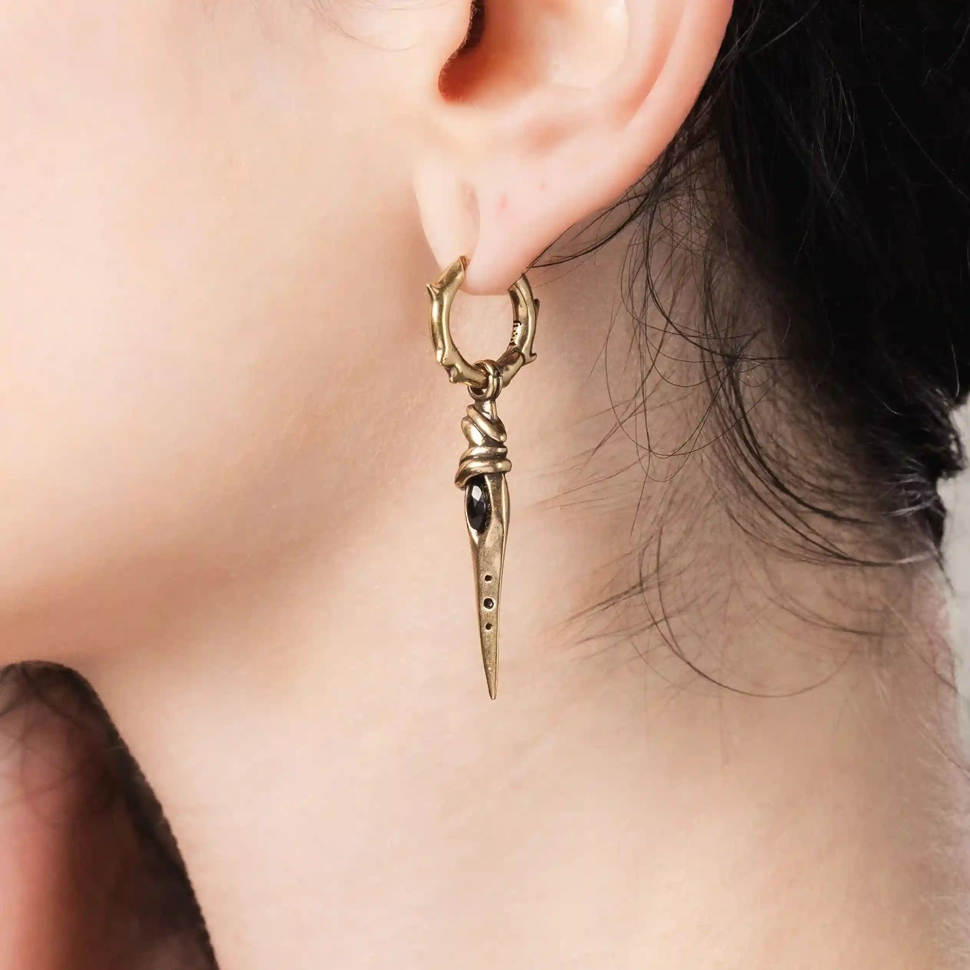 Model wearing gold Eye Dagger Earrings with long dagger drops and hammered hoop design
