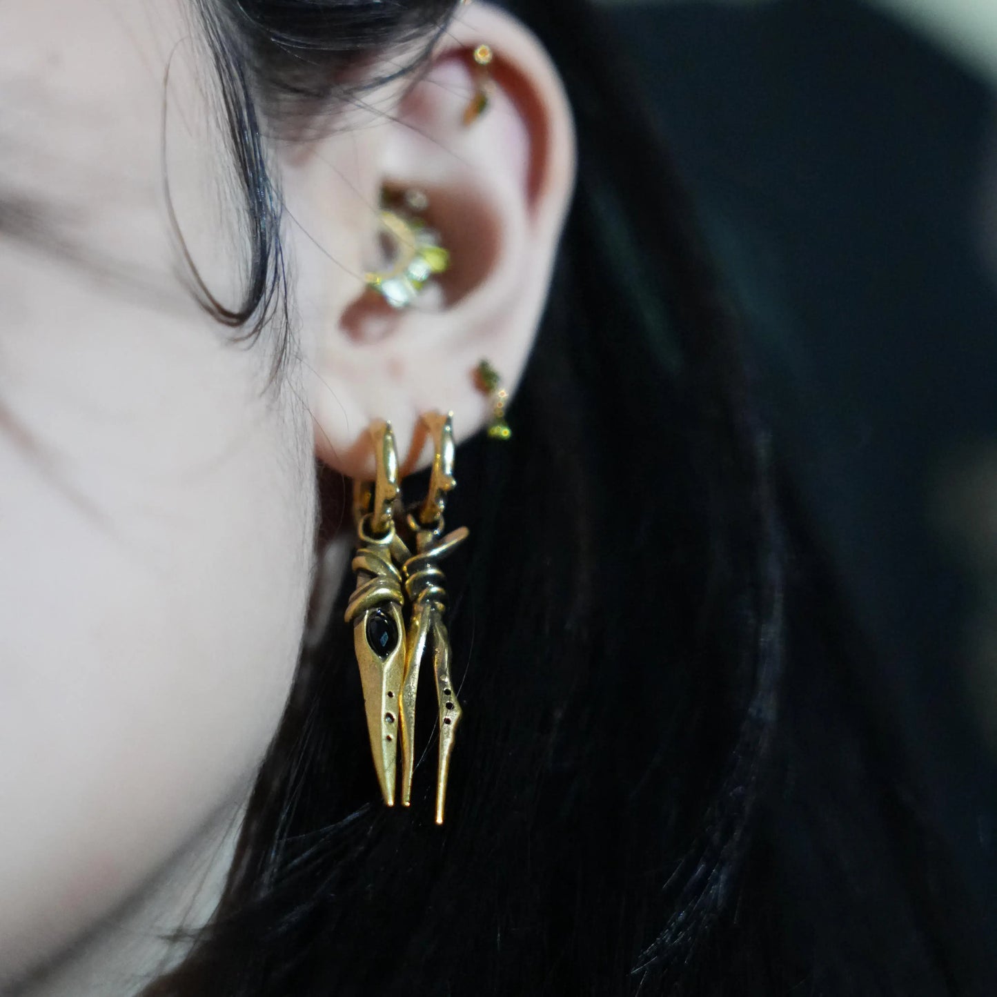 Model wearing the gold Eye Dagger Earrings with black obsidian eye-shaped stones, slim dagger drops, and bold gothic ear styling.