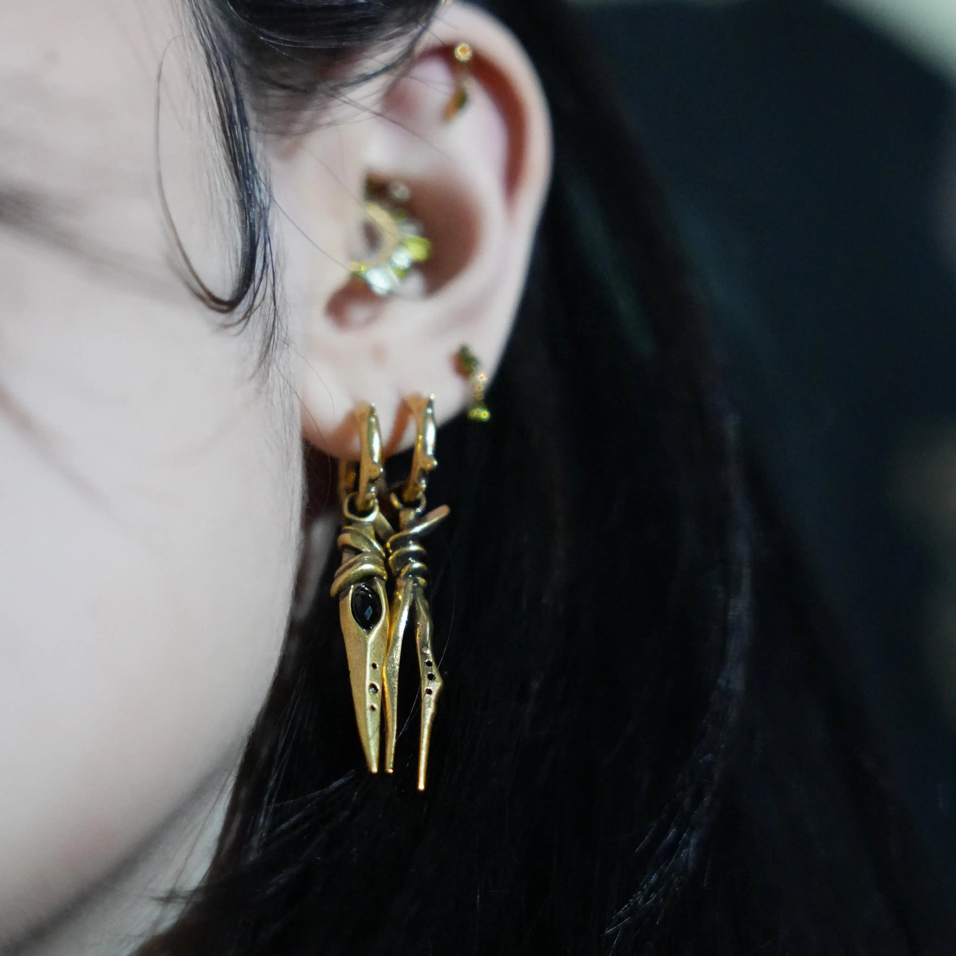 Model wearing the gold Eye Dagger Earrings with black obsidian eye-shaped stones, slim dagger drops, and bold gothic ear styling.