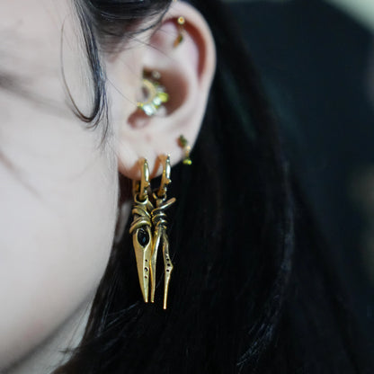 Model wearing the gold Eye Dagger Earrings with black obsidian eye-shaped stones, slim dagger drops, and bold gothic ear styling.