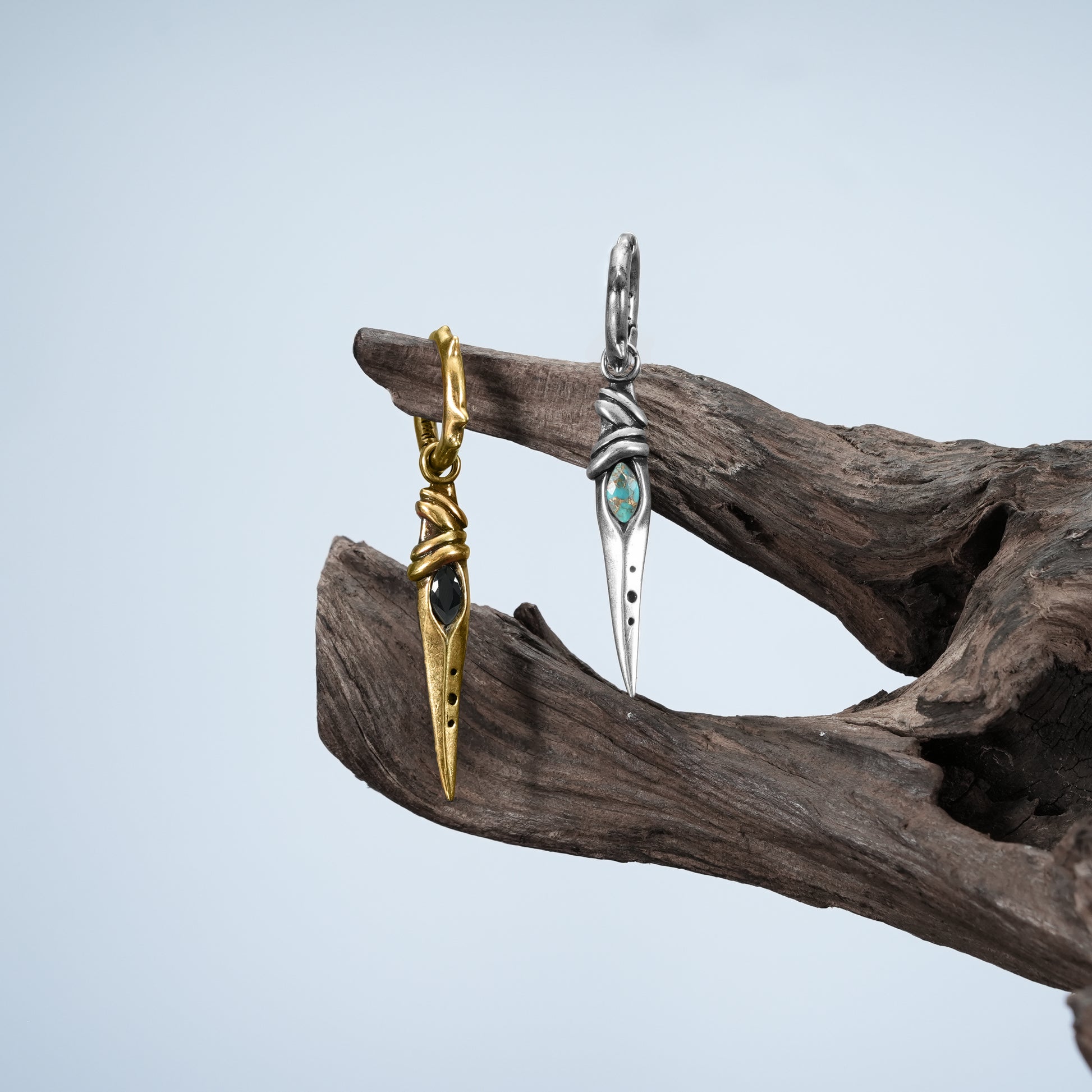 Eye Dagger Earrings in silver and gold displayed on driftwood with gothic relic styling
