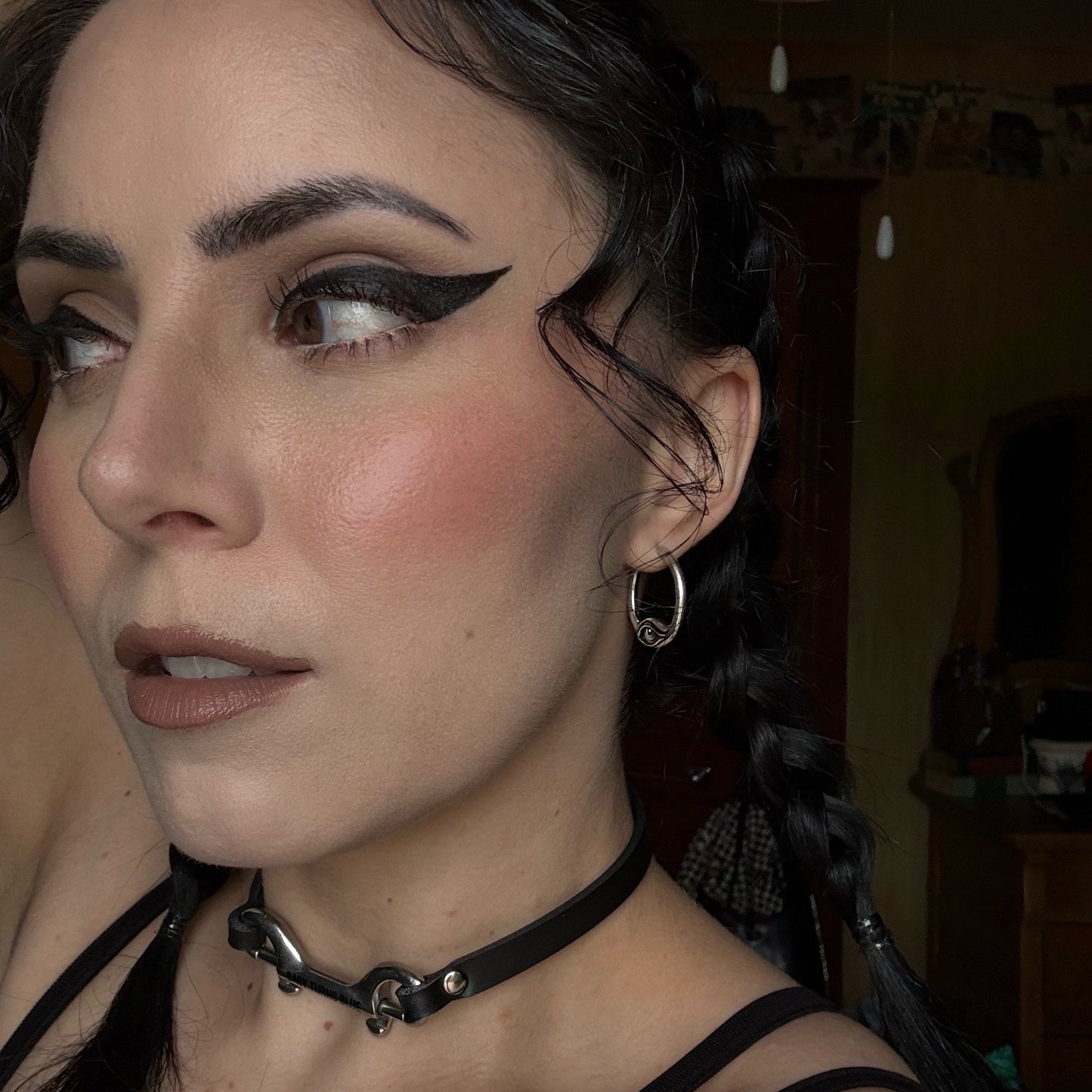 Small silver hoop earring with an eye detail worn by a model with dark hair and dramatic eye makeup