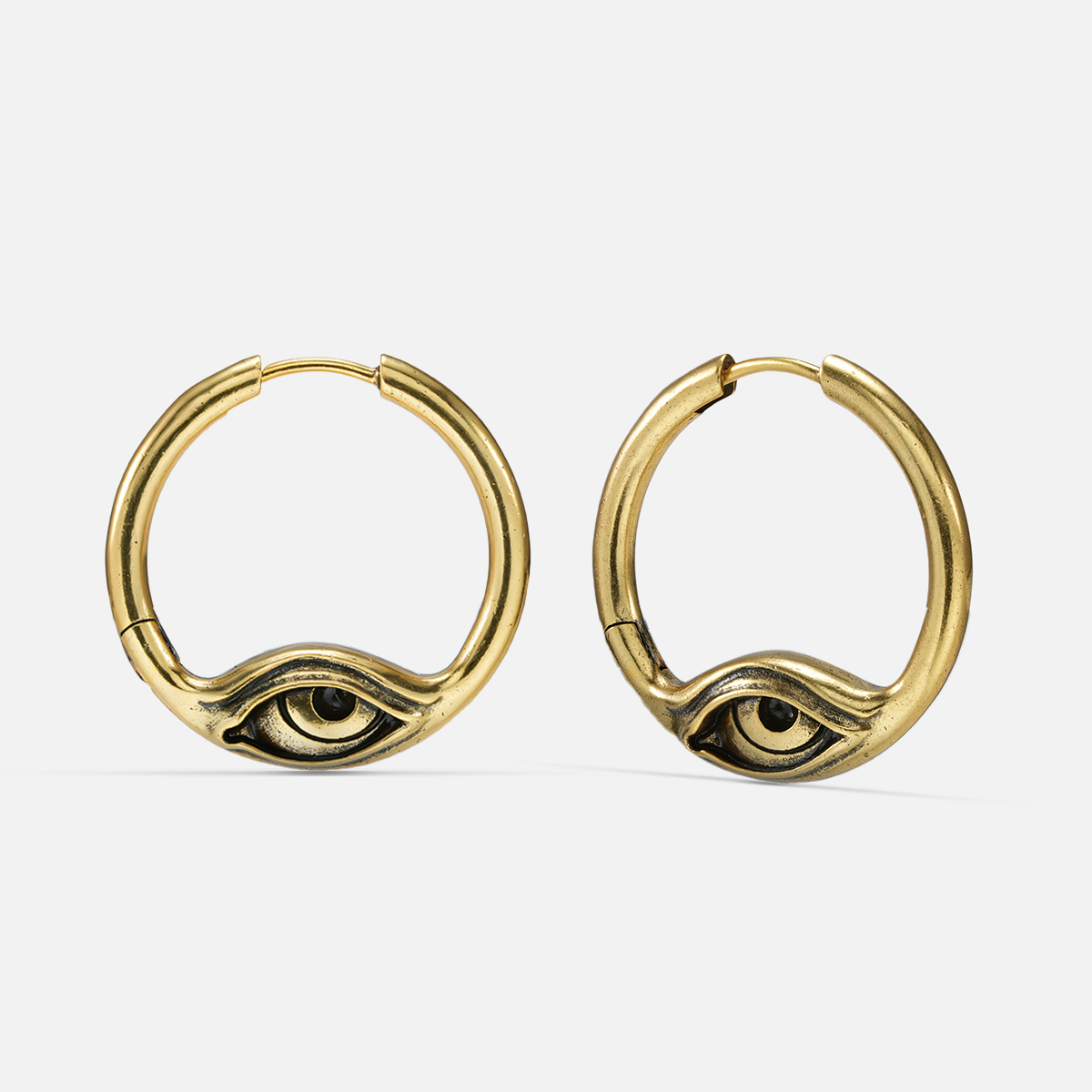 Pair of gold-tone hoop earrings featuring an engraved eye motif, front view on a flat surface