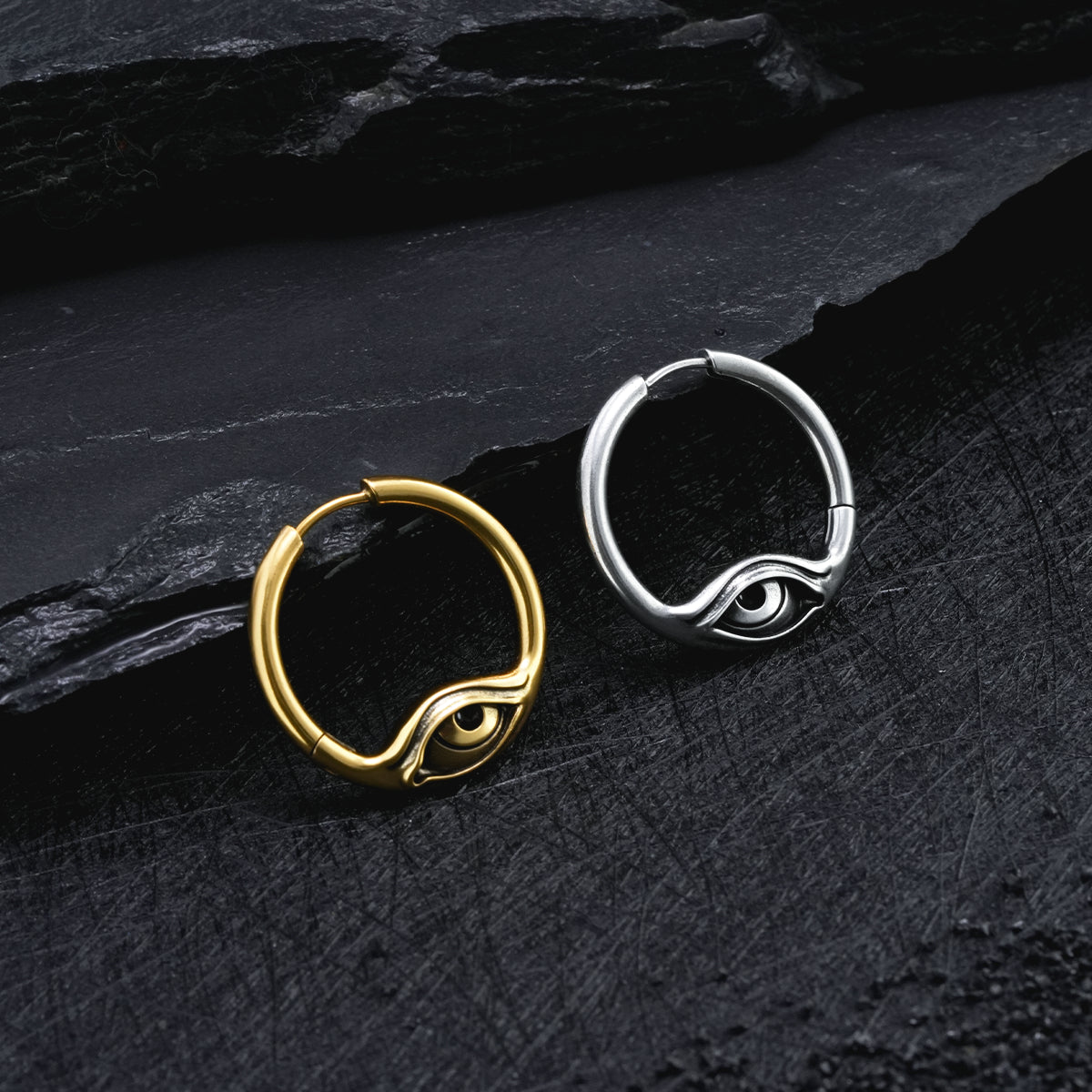 Gold and silver-tone Eyelock hoop earrings resting side by side on a textured black surface