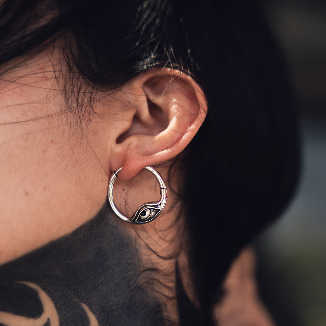 Silver-tone hoop earring with an eye motif worn on a model, close-up side view of the ear