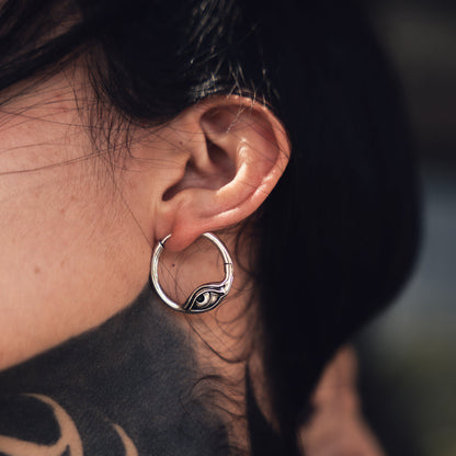 Silver-tone hoop earring with an eye motif worn on a model, close-up side view of the ear