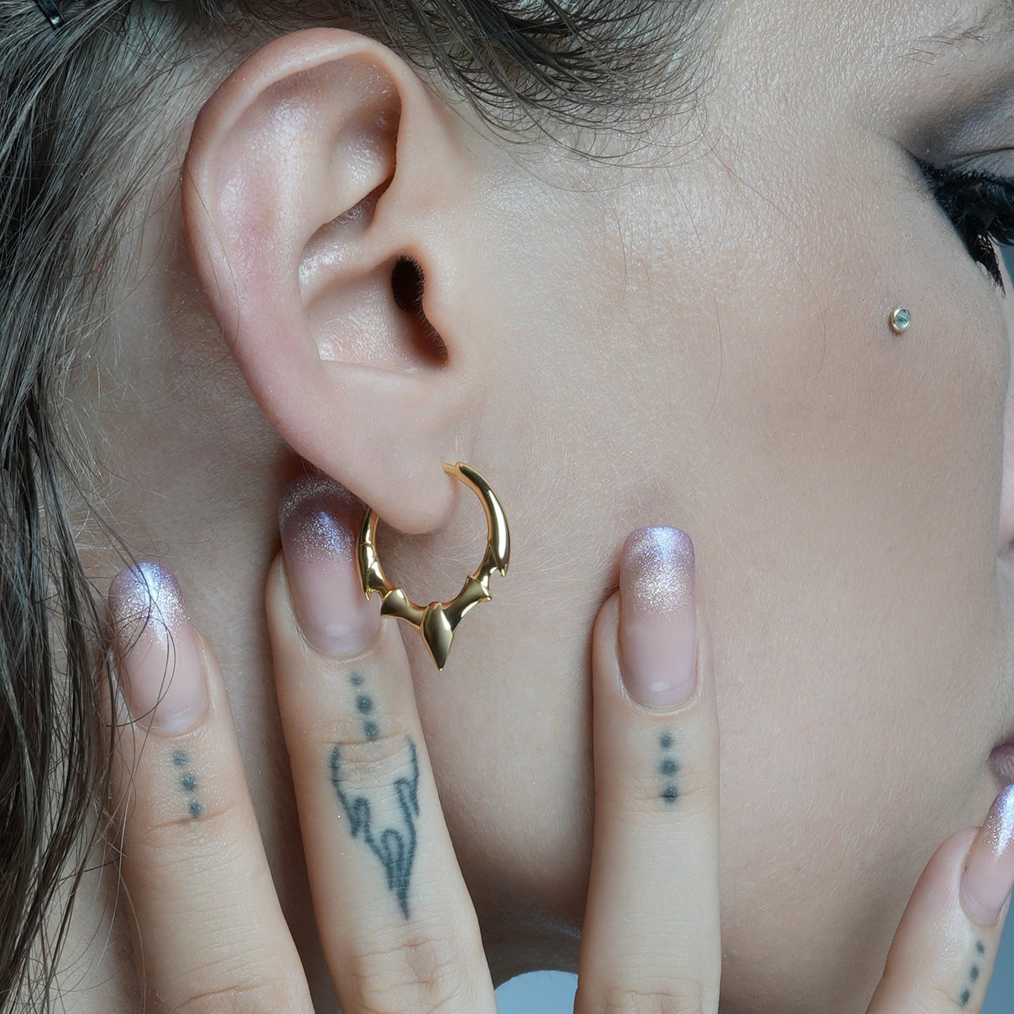 Gold-tone hoop earring with fang-shaped crest detail worn on model's ear, close-up view