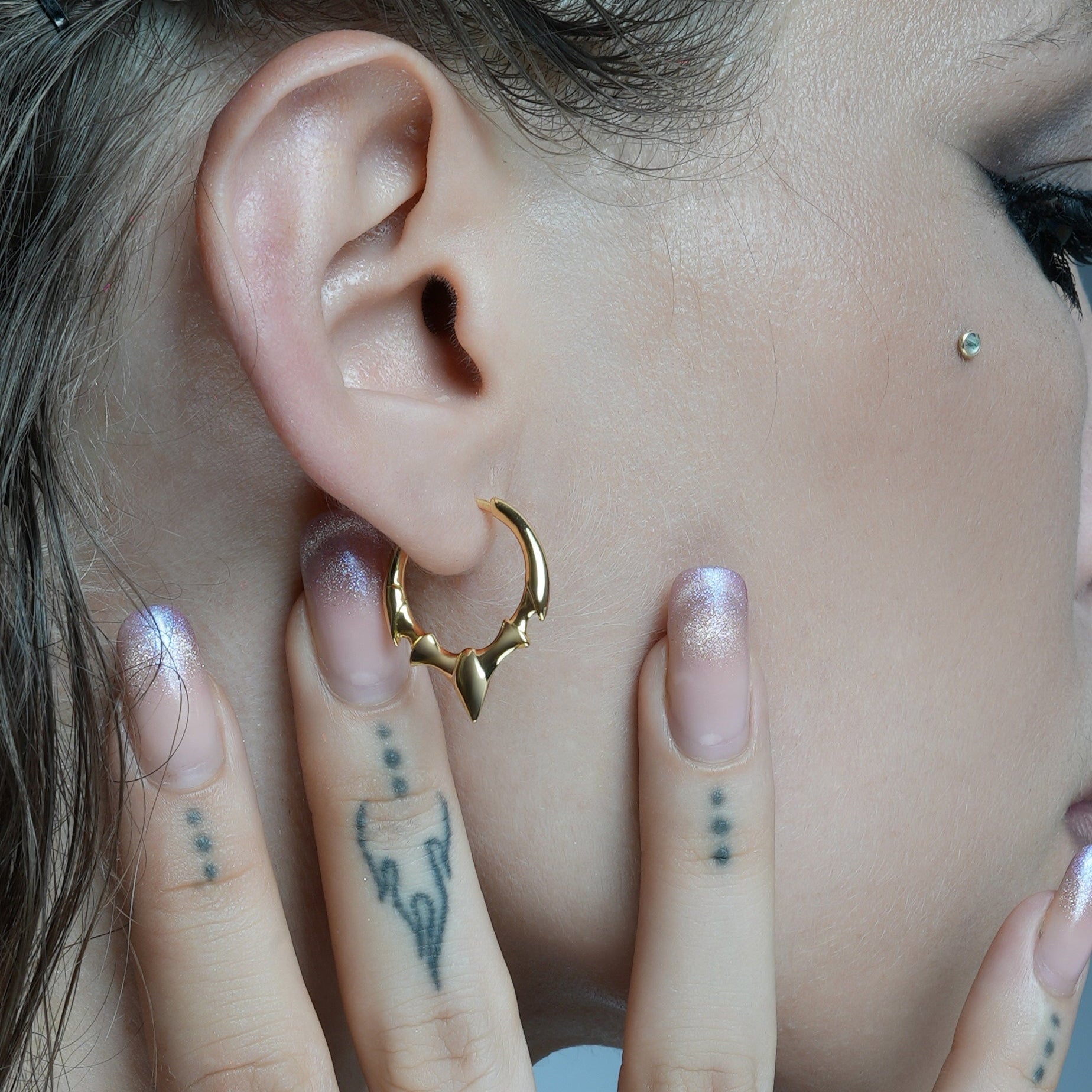 Gold-tone hoop earring with fang-shaped crest detail worn on model's ear, close-up view